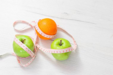 Beyaz arka planda izole edilmiş iki yeşil elma ve portakala sarılı şerit, kilo verme hedefi kavramı, diyetin amacı