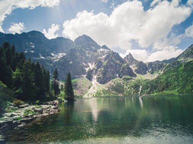 Dağlardaki güzel alp gölü, doğal arka plan, mavi bulutlu gökyüzü ile yaz manzarası ve kristal berrak su yansıması, Morske Oko, Tatra Dağları, Zakopane, Polonya