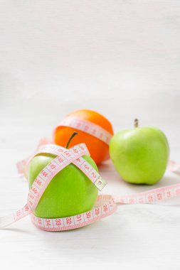 Beyaz arka planda izole edilmiş iki yeşil elma ve portakala sarılı şerit, kilo verme hedefi kavramı, diyetin amacı