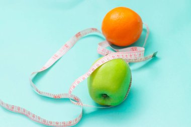 Beyaz arka planda izole edilmiş iki yeşil elma ve portakala sarılı şerit, kilo verme hedefi kavramı, diyetin amacı,