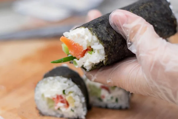 Cook's hands close-up. A chef makes sushi and rolls from rice, red fish, avocado and philadelphia cheese. step by step