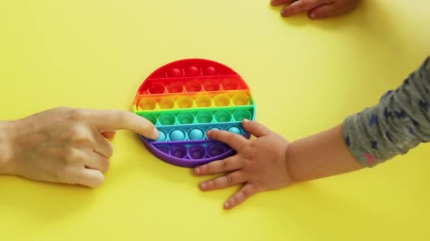 Antistress pop it toy. hands of mom and baby play New popular silicone colorful antistress popit toy for child on yellow background. View from above. — Stock Video