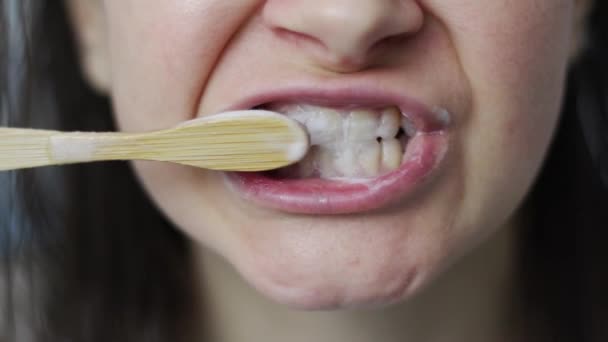 Uma jovem escova os dentes com uma escova de madeira de bambu. Conceito de produtos biodegradáveis. Conceito de resíduo zero. — Vídeo de Stock
