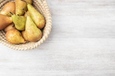 Hasır sepetin içindeki olgun armutlar ahşap masa, üst manzara, lezzetli meyve suyu hasadı.,