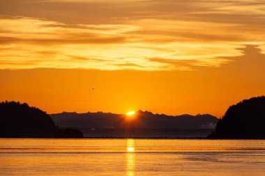 Önünde su olan iki tepenin arasından yükselen dramatik güneş..