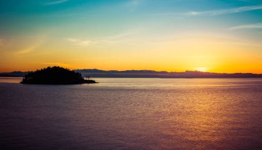 Gün batımında küçük bir adada, renkli bir gökyüzüyle...