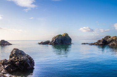Etrafındaki mavi okyanus sularından çıkan kayalar.