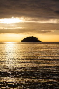 Gün batımına karşı gölgeli küçük bir ada ve suda bir sürü renkli yansıma..