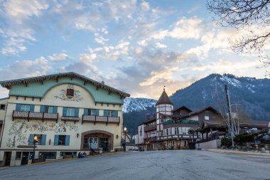 Bauernhaus style Bavarian buildings with snow covered mountains in the distance in the town of Leavenworth, Washington. clipart