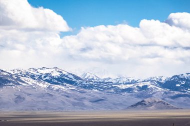 Idaho 'da uzak karla kaplı dağ zirveleri beyaz bulutlar ve mavi gökyüzü.