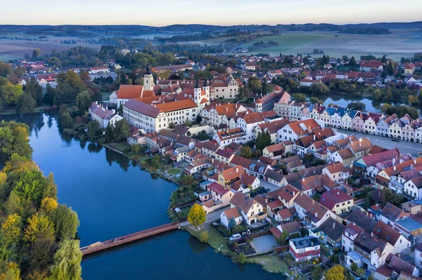 Aerial view before sunrise of the Telc Castle with foreground bridge, pond and rolling hills in the Czech Republic.