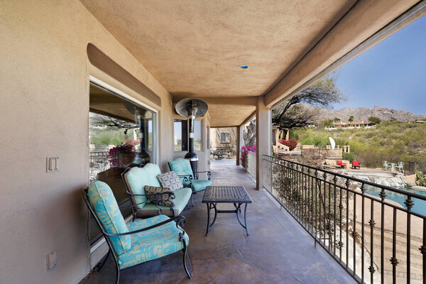 Sitting area on a balcony overlooking a terraced patio with swimming pool in a desert environment.