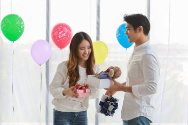 Mutlu yıllar, Noel ve Çift Kavramı. Asyalı genç adam ve kadının portresi arka planda renkli balonu olan bir adamın hediye kutusundaki ayı bebeğiyle şaşırdı..