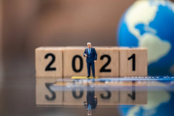 2021 Global Business Money and Financial concept. Businessman miniature figure people standing on credit card with wooden number block and mini world ball as background.