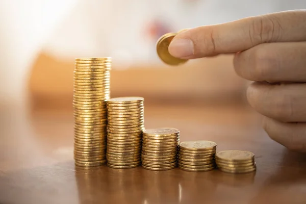 Business, Money, Finance, Secure and Saving Concept. Close up of man hand holding and put coin to stack of gold coins on wooden table.