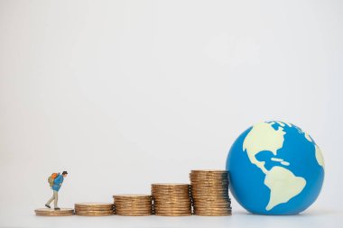 Küresel İş Seyahat ve Tasarruf Konsepti. Sırt çantalı gezgin minyatür. Beyaz arka planda mini dünya topu olan altın sikkeler üzerinde yürüyor..