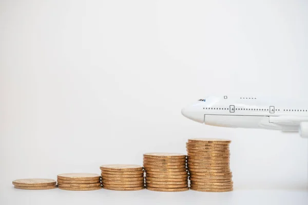 Business, Money and Travel Concept. Closeup of airplane model with stack of gold coins on white background.