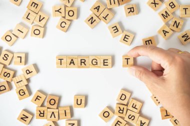 İş kavramı. Beyaz arka plandaki diğer İngilizce harf bloklarıyla birlikte TARget yazımını tamamlamak için T ahşap harf bloğunu tutan adama yaklaş.