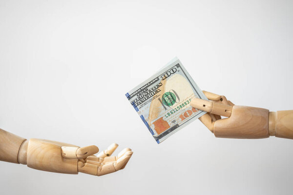 Концепция денежных средств и платежей. Поднять деревянную модель руки и отдать стодолларовую купюру в другую руку.