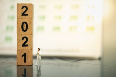2021 Yeni Yıl Sağlık ve İş Konsepti. Doktor minyatür figür. Arkaplan olarak ahşap blok ve takvim yığını ile yerde yürüyen insanlar..