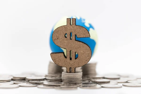 Global Business and Money Concept. Closeup of wooden US Dollar sign on stack of silver coins with mini world ball as background.