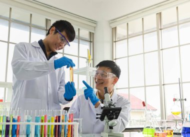 Profesyonel kıdemli doktor, laboratuvarda turuncu sıvı maddeyle test tüpü arayan genç bilim adamına öğretiyor ve rehberlik ediyor..