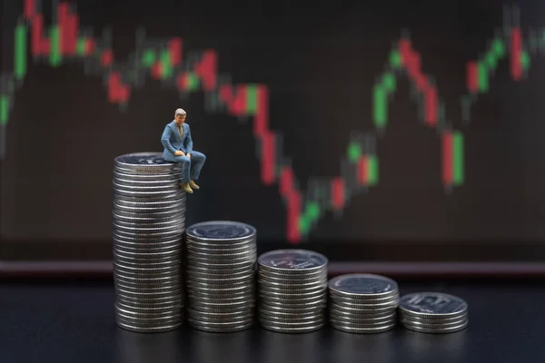 Business Money and Financial Concept.Businessman miniature figure people sitting on stack of silver coins with candlestick chart as background.