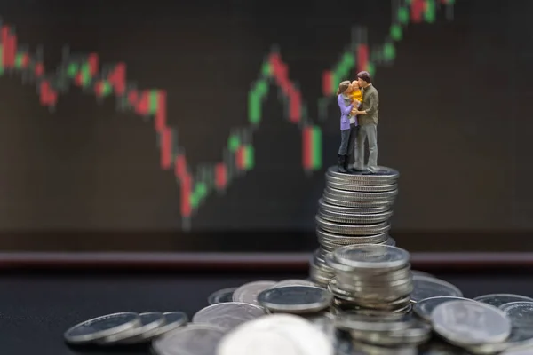 Money, Financial, Business Investment and Family concept. Parent and child Miniature figures hug and kiss together standing on stack of coins with candlestick chart as background.
