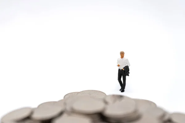 Business, Money Investment and Planning Concept. Businessman miniature figure people figure walking to pile of silver coins on white background.