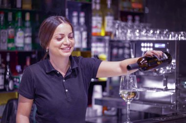 Barmen kadın beyaz şarap dolduruyor. Barmen çalışıyor.