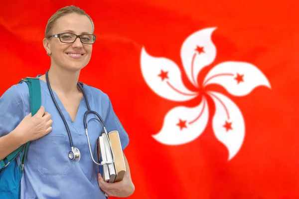 Female student doctor with stethoscope and books in hand on the Hong Kong flag background. Medical education concept. Medical learning in Hong Kong