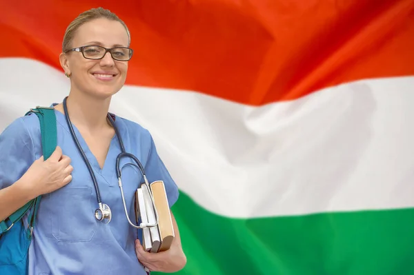 Female student doctor with stethoscope and books in hand on the Hungary flag background. Medical education concept. Medical learning in Hungary