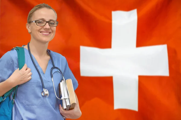 Female student doctor with stethoscope and books in hand on the Switzerland flag background. Medical education concept. Medical learning in Switzerland