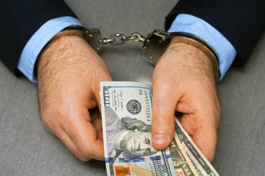 Ellerinde dolar banknotları tutan iş adamı kelepçeleri. Elleri kelepçeli bir memur rüşvetle