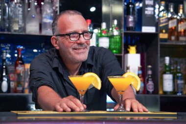 Barda kokteyl servisi yapan gözlüklü yaşlı bir barmen. Akşam vakti.