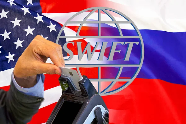 Flag of USA and Russia flag and text of SWIFT. Hand of woman with credit card in payment terminal. Society for Worldwide Interbank Financial Telecommunications, online payment and financial regulation sanctions concept