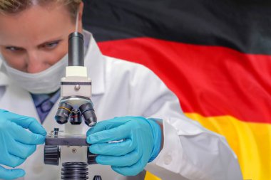 Kadın biyokimyacı mikroskopla Almanya bayrağı arkaplanına bakıyor. Almanya 'da tıp teknolojisi ve farmasötik araştırma ve bilim kavramının geliştirilmesi