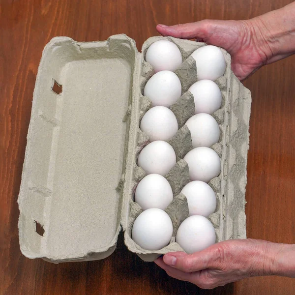 Hands old woman with packages of white eggs in the home. Elderly woman buys eggs. Buying eggs at the grocery store