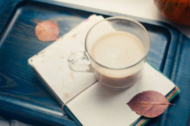 Bir balkabağı kabağı ve bitki bazlı yulaf ezmesi ya da boş not defterli badem sütü ile yapılmış latte kahve. Masada koyu mavi desenli fotokopi alanı çalışma konsepti üzerine.