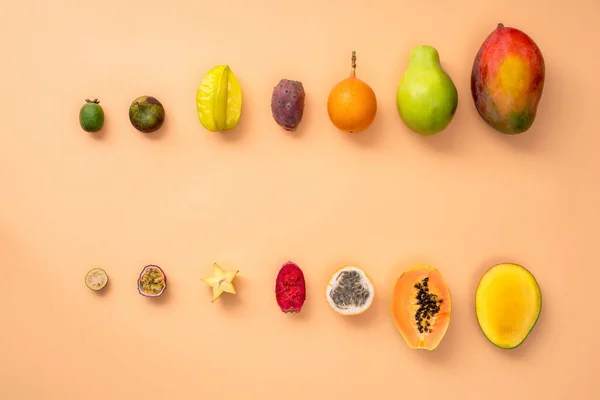 Fresh tropical whole and halved fruits on a beige background making a row.