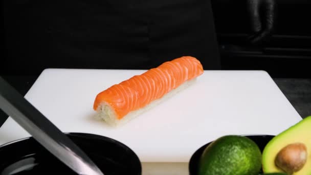Chef schneidet Sushi-Rollen mit einem Messer auf weißem Brett. — Stockvideo