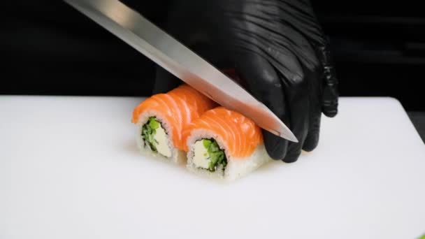 Chef snijden rollen sushi met een mes op een wit bord. — Stockvideo