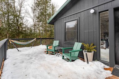 Livingston Malikanesi New York Şubat 2025: Kar, Sullivan County 'de kış boyunca yeşil Adirondack sandalyeleri, hamak ve siyah kulübe ile kaplıydı.