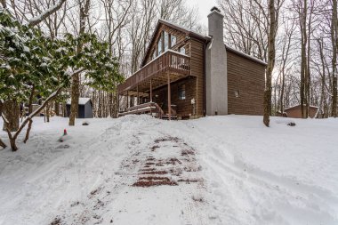 Poconos, PA / USA 10 Şubat 2024: Poconos 'ta kırsal bir ahşap kulübenin yanında karla kaplı açık hava güvertesi. Sahne, çıplak ağaçlarla, ahşap piknik masasıyla sakin bir kış manzarasını gösteriyor..