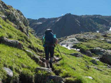 Stubai yürüyüş parkurunda ağır sırt çantalı yalnız adam yürüyüşçüsü, Stubai Hohenweg yeşil yaz dağ vadisinde bahar deresi ile. Tyrol, Avusturya Alpleri