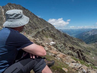Dağ vadisine ve Stubai yürüyüş parkurundaki karlı tepelere bakan yürüyüşçü, Bremer kulübesi ile Stubai Hohenweg. Tyrol, Stubai Alpleri, Avusturya Yaz Kayalık Alp manzarası