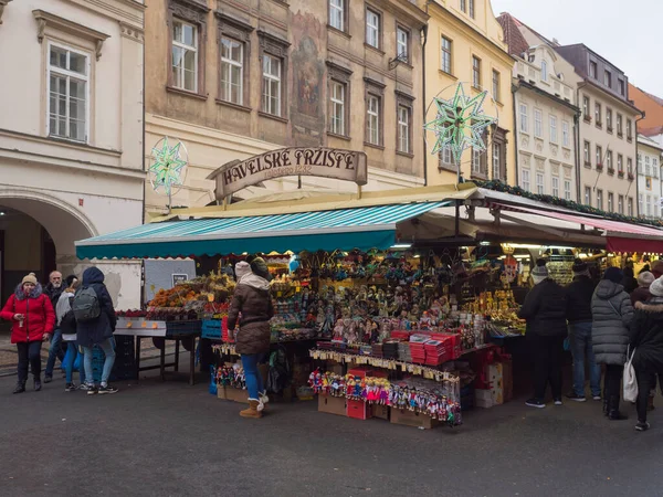 Praga, Czechy, 12 grudnia 2019: Turyści kupujący na tradycyjnym jarmarku bożonarodzeniowym, ul. Havelska trznice ze straganami z prezentami, pamiątkami, ozdobami świątecznymi, zabawkami i owocami. — Zdjęcie stockowe