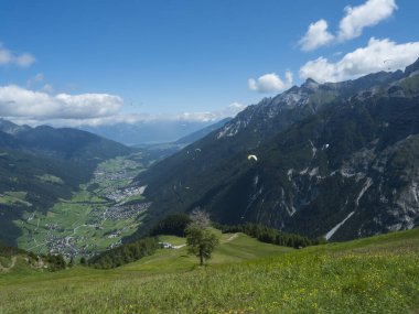View over green Stubai valley and Neustift im Stubaital village from Elferhutte with moutain peaks and kites. Tirol Alps, Austria, Summer blue sky, white clouds