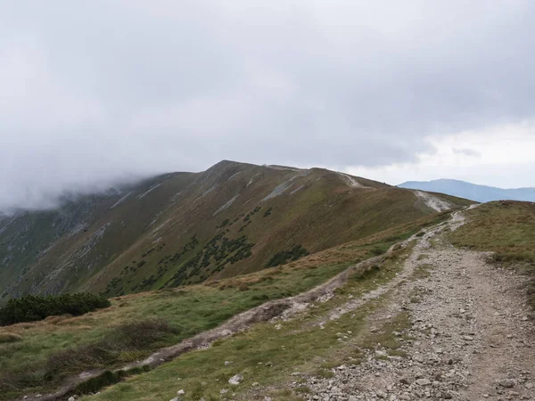 Sendero de senderismo desde Chopok en el prado de la montaña, laderas de colinas cubiertas de hierba con niebla gruesa y nubes. Baja cresta de las montañas Tatras, Eslovaquia, fines de verano día ventoso — Foto de Stock