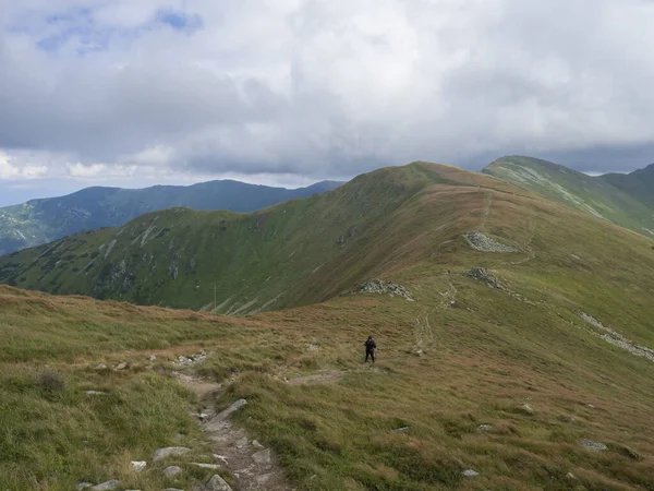 Çimenli dağ sırtlarında yürüyüş yolunda yürüyen yalnız yürüyüşçü, kötü havada yamaçlarda güçlü rüzgar, kalın sis ve bulutlar, Chopok, Low Tatras, Slovakya, yaz günü geç saatlerde — Stok fotoğraf